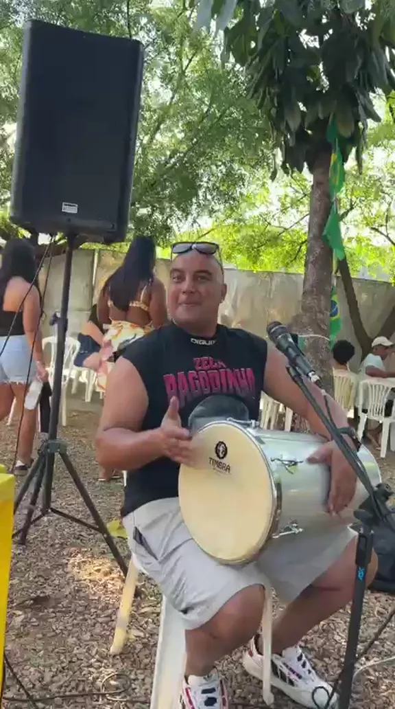 Integrante tocando tantã sentado, com caixa de som ao lado